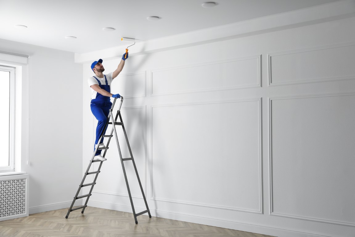 Handyman painting ceiling with white dye indoors, space for text